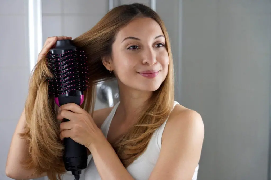 Girl using brush hair dryer to style hair at the mirror on bathroom