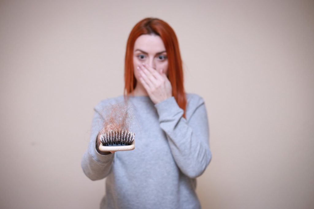 Woman holding a hairbrush with her hair on it to show that it is falling off a lot.